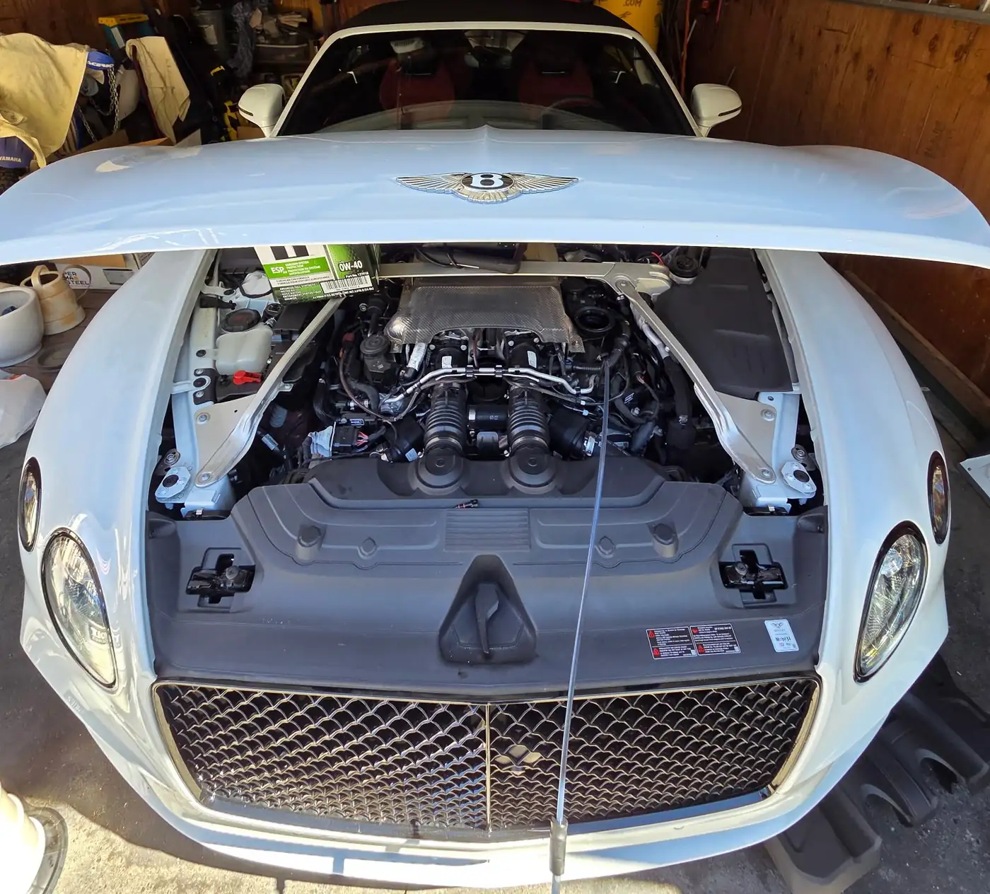 A white Bentley coupe with the hood up in a garage, the engine bay exposed