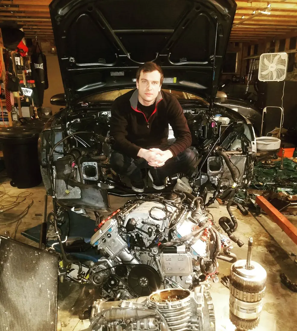 Maksim Yakovlev crouched in his garage beside an engine lifted out of a car, tools and parts around him